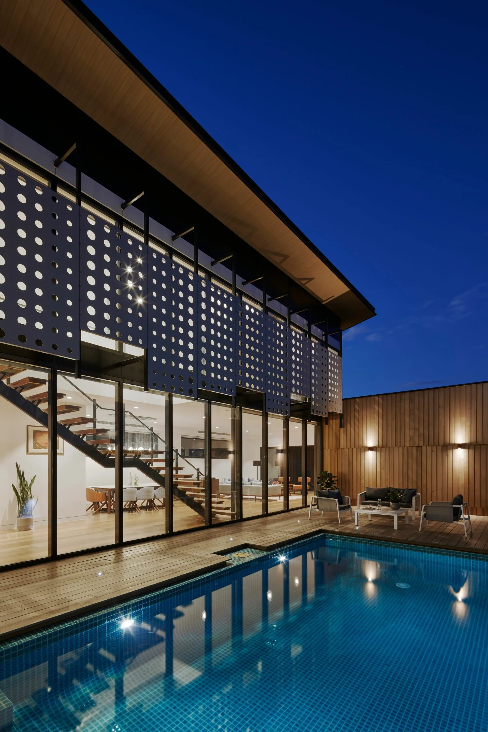 Casa moderna de noche con fachada de celosía, alberca iluminada y deck WPC