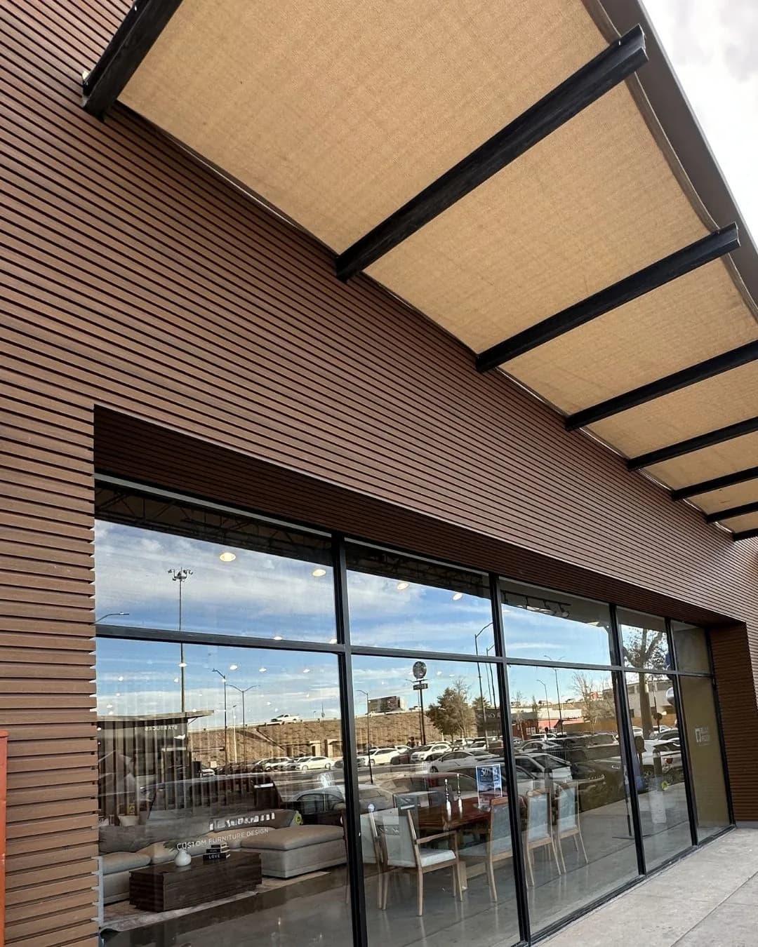 Fachada comercial revestida de lambrín WPC horizontal tono madera sobre un aparador de cristal, bajo un toldo, vista desde la banqueta