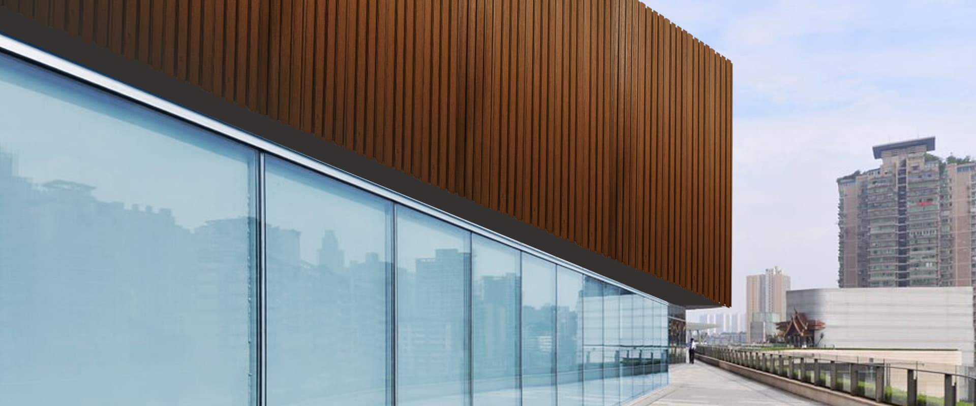 Muro de lambrín WPC tono madera sobre una fachada de cristal que refleja edificios