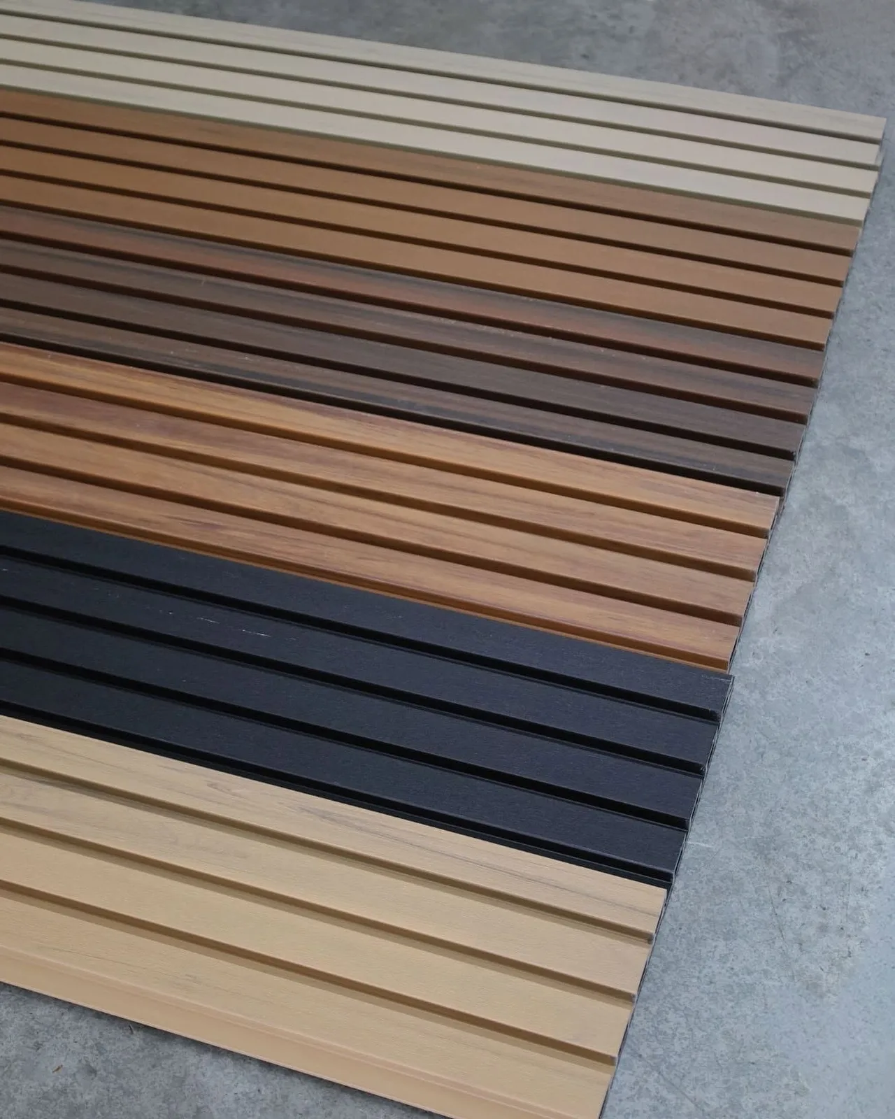 Tablas de lambrín WPC ranurado en varios colores, acomodadas una junto a otra sobre un piso de concreto