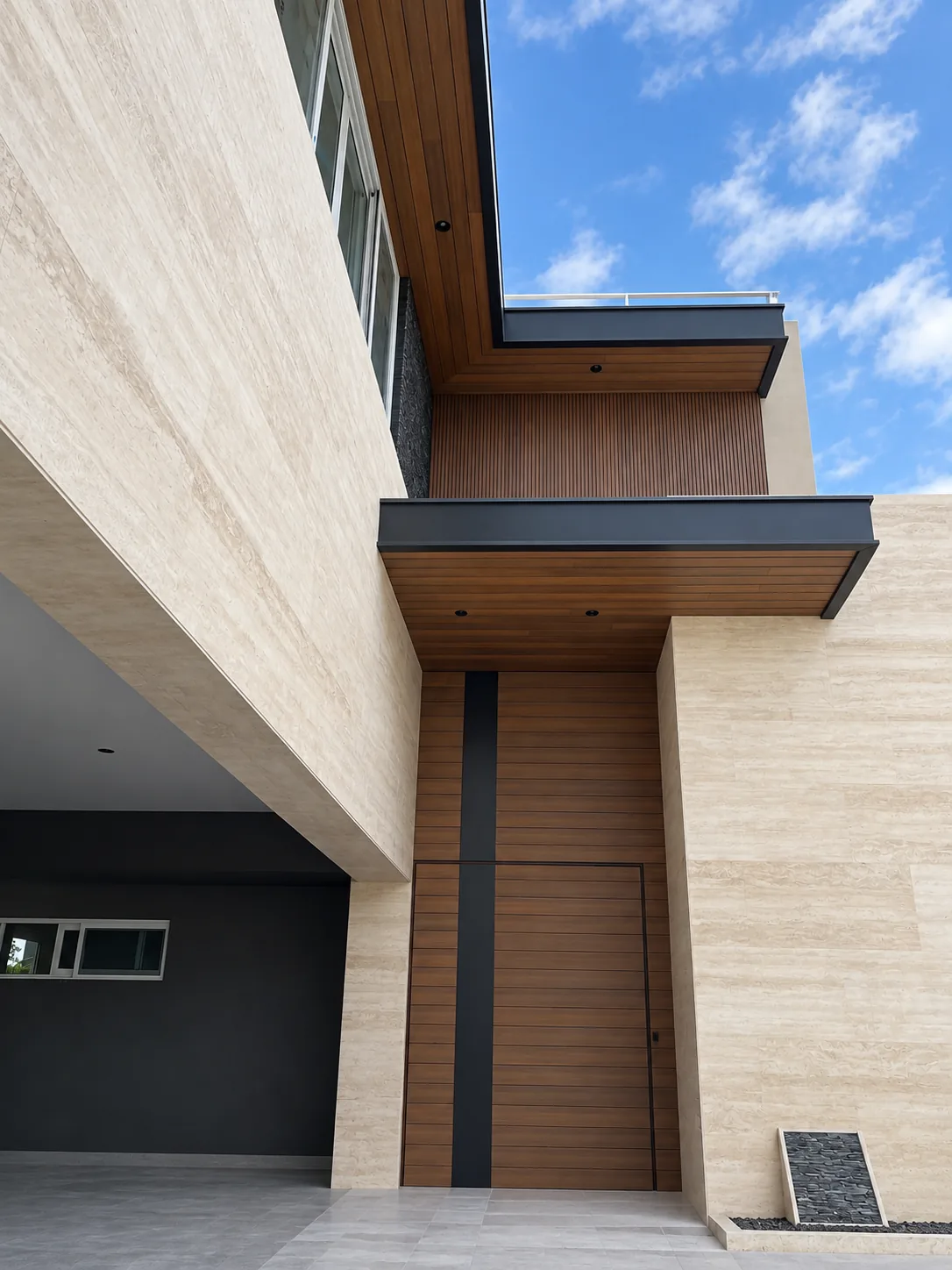 Acceso de una casa con Wall Cladding WPC tono madera bajo los volados de la fachada, entre muros de piedra clara