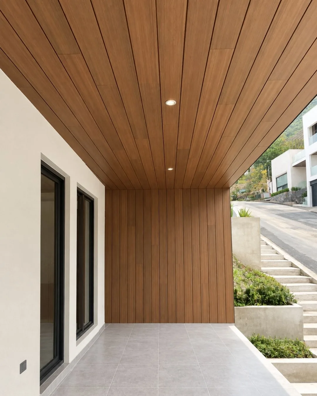 Pórtico de una casa con el techo y el muro del fondo revestidos de Wall Cladding WPC tono madera, luces empotradas y una escalera exterior al lado